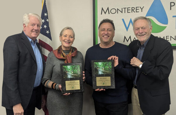 Four individuals stand together, holding awards in front of a sign for Monterey Peninsula Water Management. An American flag is visible in the background.